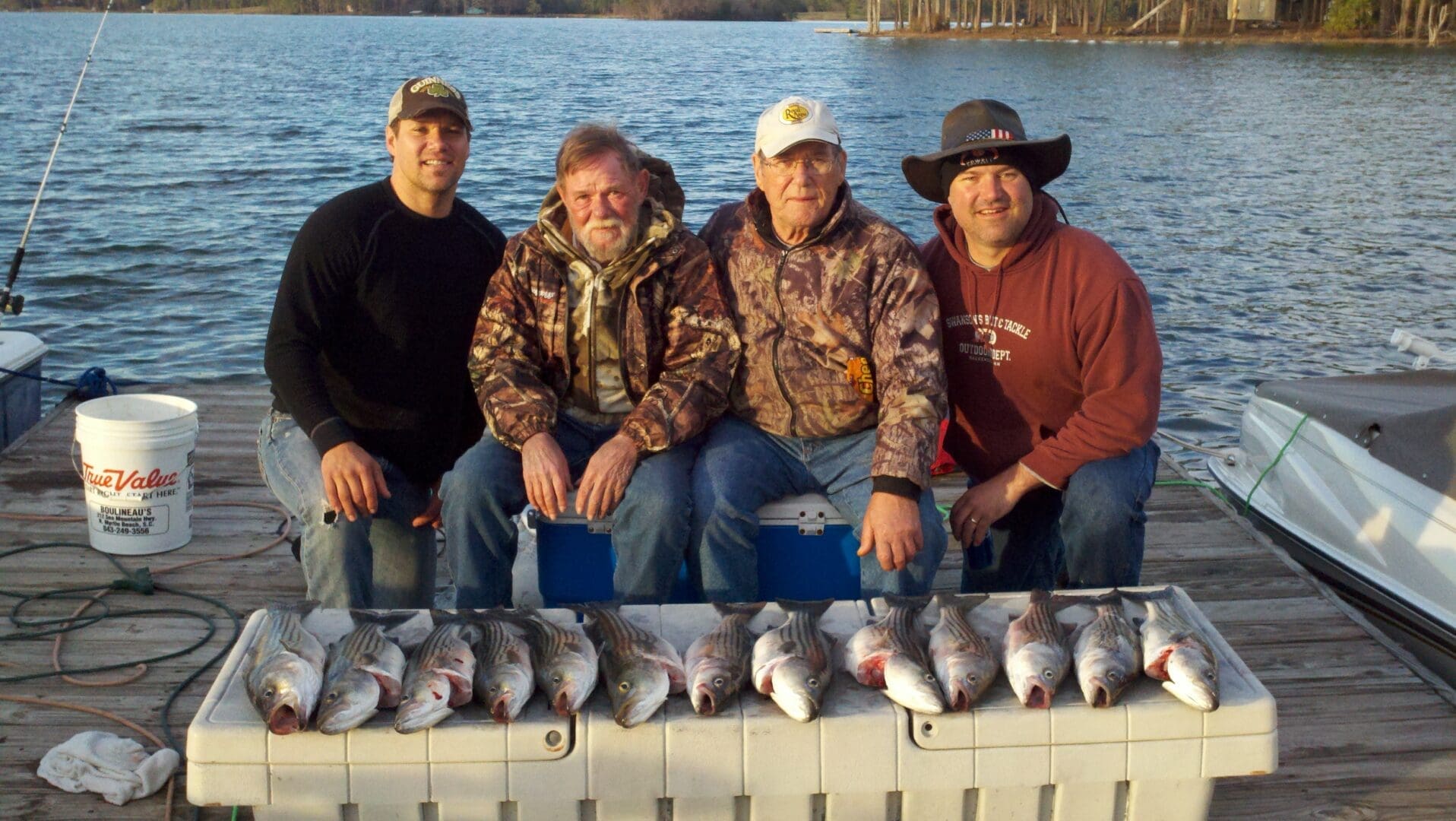 Four men sitting on a ledge with fish.